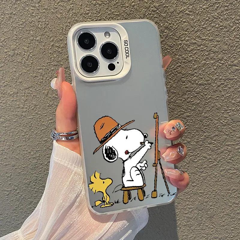 Frosted clear phone case featuring Snoopy as an artist, wearing a brown hat while painting at an easel.  Woodstock watches nearby in this charming Peanuts cartoon design, showcased in a hand with glitter nail polish.